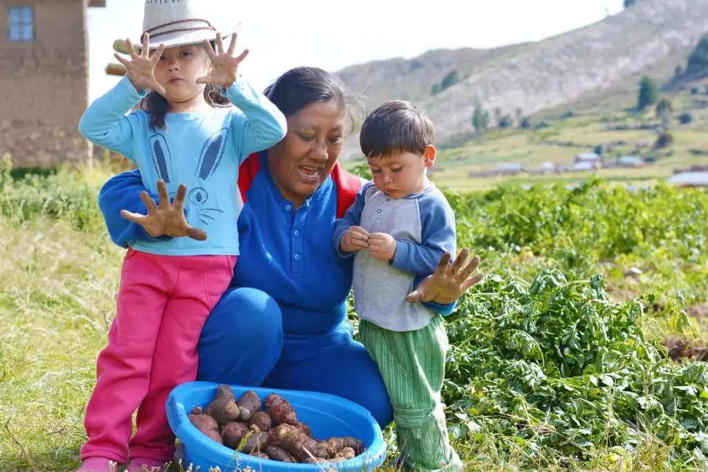 A smiling woman crouching in a field with two small children and a basket of potatoes