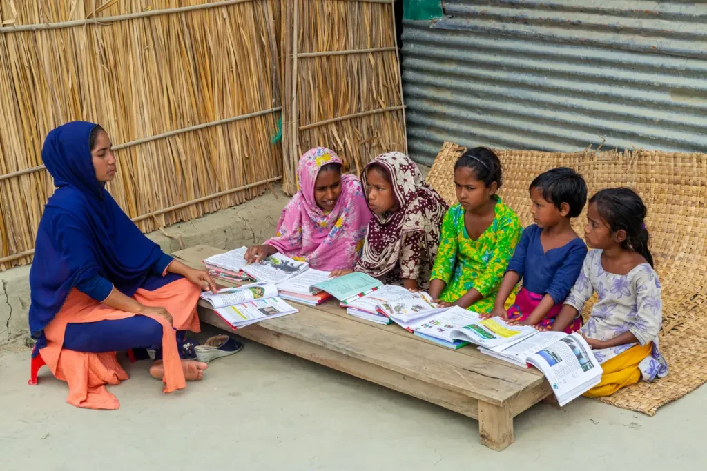 A woman sharing picture books with a group of girls seated on a mat